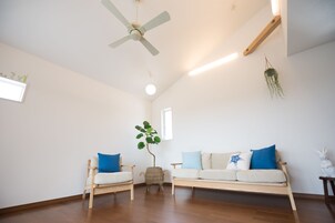 Un salón amplio con techo alto, ventilador de techo y dos sofás con cojines azules.