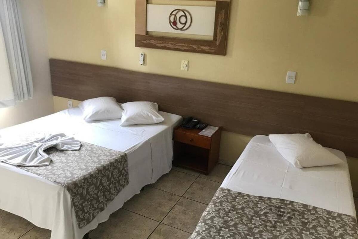 A hotel room with two beds, a wooden headboard, a framed artwork on the wall, and a bedside table with a phone.