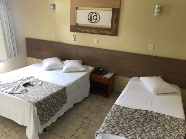 A hotel room with two beds, a wooden headboard, a framed artwork on the wall, and a bedside table with a phone.