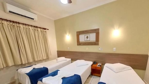 Una habitación de hotel con dos camas individuales, una mesita de noche, un equipo de aire acondicionado y un cuadro enmarcado en la pared.