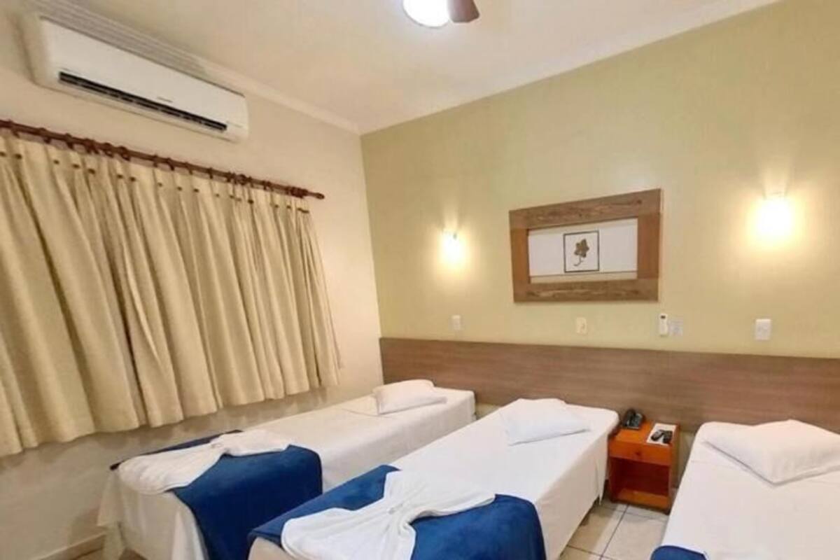 A hotel room with two single beds, a nightstand, an air conditioning unit, and a framed picture on the wall.