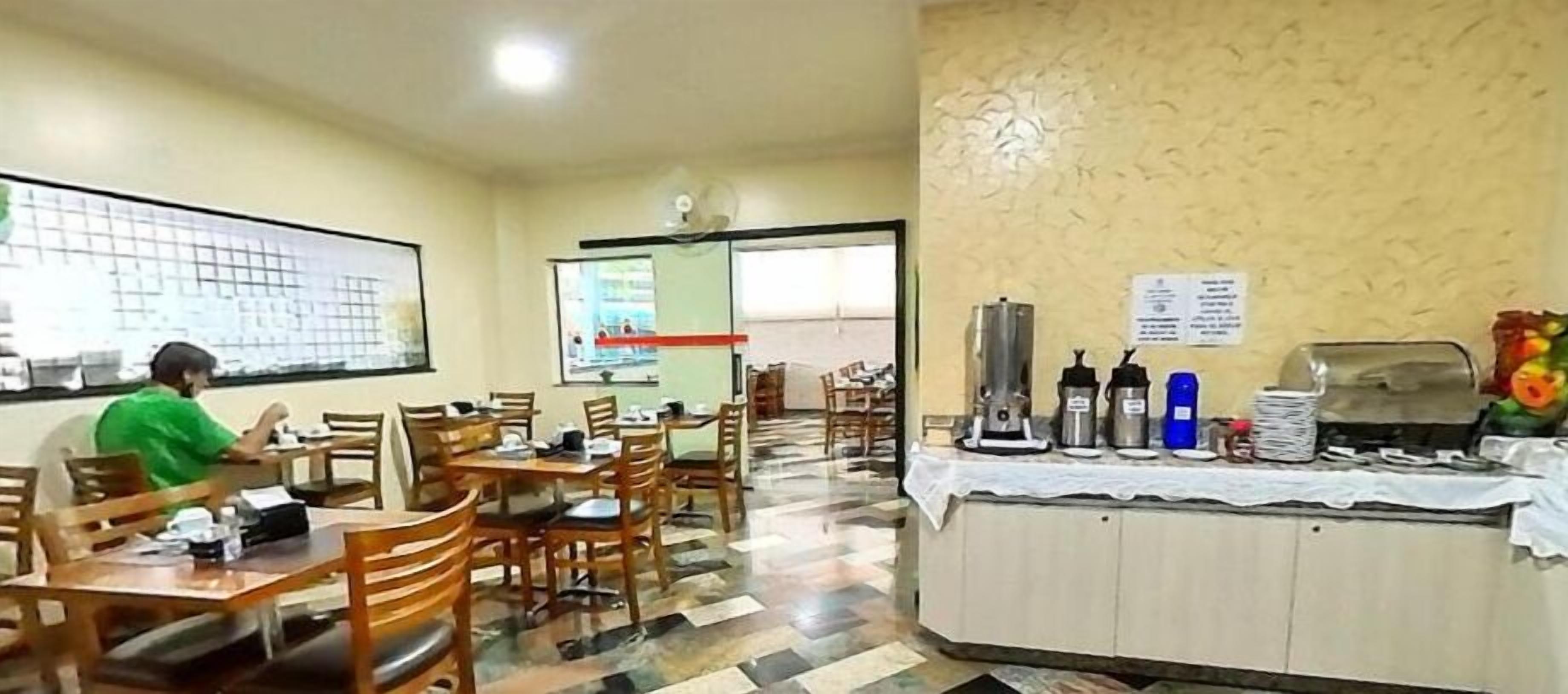 A dining area with wooden tables and chairs, a buffet counter with food and drink dispensers, and a projector screen on the wall.