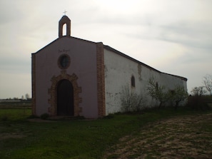 A small, single-story building with a cross on top, a circular window, and a brick archway.