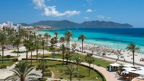 A coastal cityscape with a beach, palm trees, and a mountain in the background.