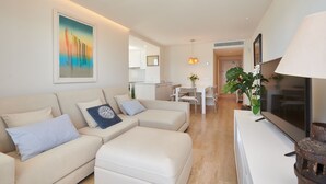 A modern living room with a beige sofa, a flat-screen TV, and a dining area in the background.