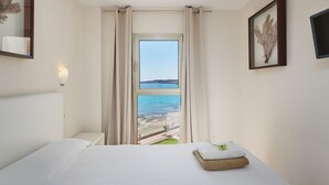 A hotel room with a bed, a window with curtains, a wall-mounted light, and a framed picture.