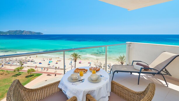 A balcony with a table set for breakfast overlooking a beach.
