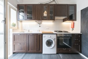 Una cocina moderna con armarios de madera oscura, lavadora integrada y horno empotrado.