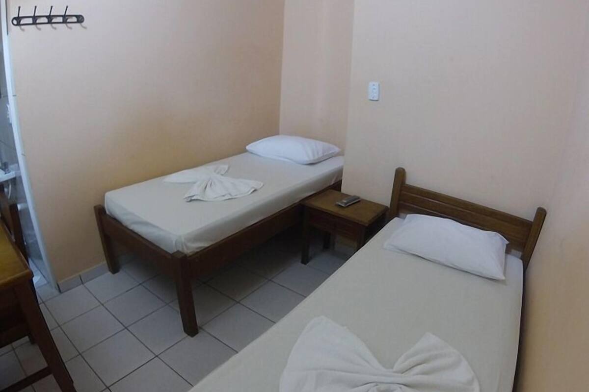 A small, clean room with two single beds, a wooden nightstand, and a simple, uncluttered design.