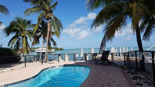A swimming pool with palm trees, a beach, and a view of the ocean.