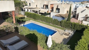 A residential area with a swimming pool, lounge chairs, and a view of the sea.