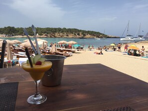 A beach scene with umbrellas, lounge chairs, and a table with a drink.