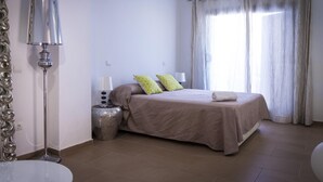 A bedroom with a bed, a bedside table with a lamp, a mirror, and a window with curtains.