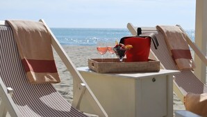 A beachside lounge with striped chairs and a table set with a drink dispenser, glasses, and a basket of fruit. - La Vue Sur La Mer Beach House (Viareggio)