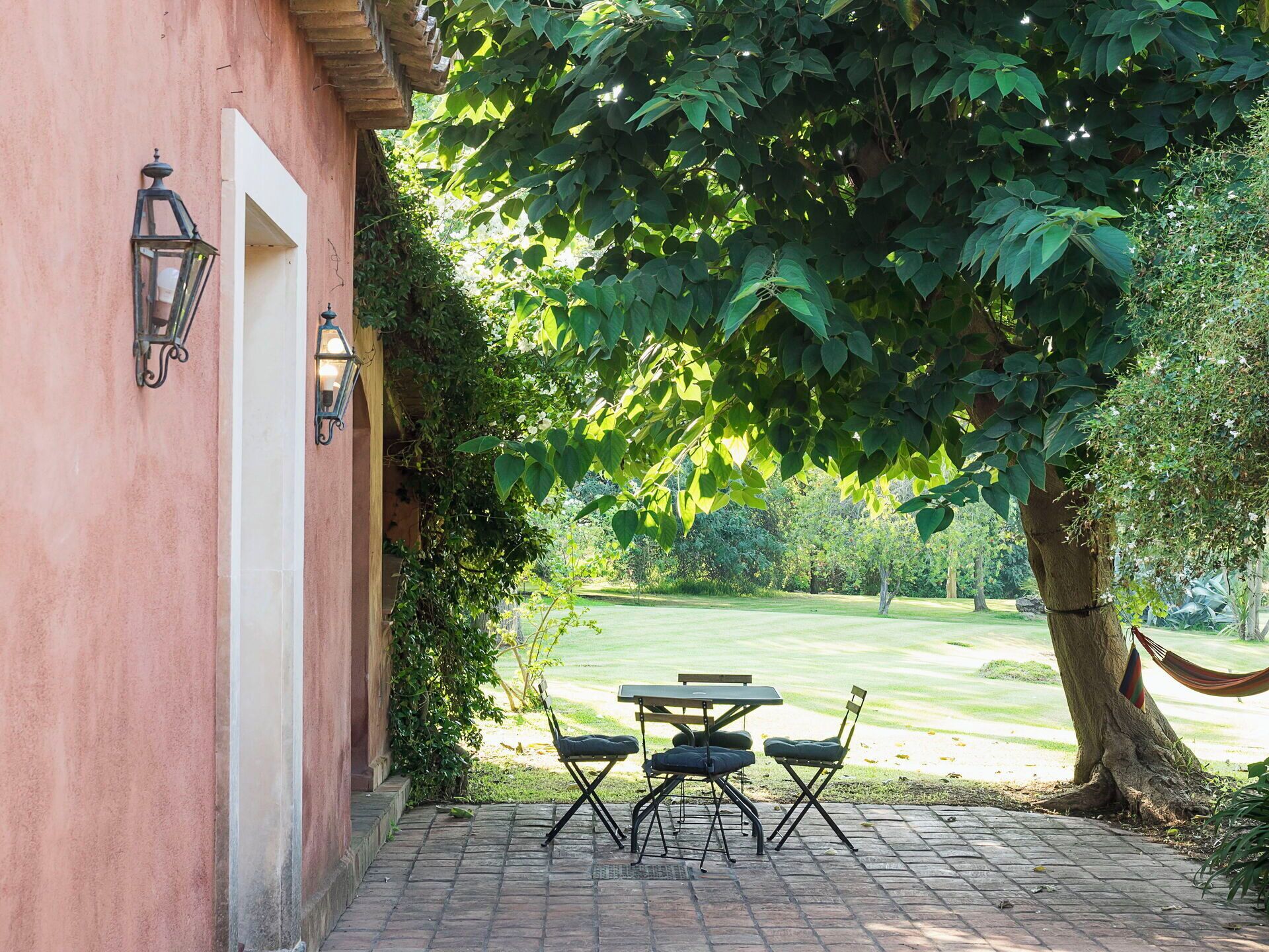 A patio with a table and chairs, a hammock, and a view of a grassy area.