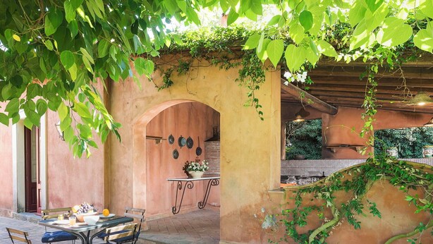 Eine Terrasse im Freien mit Tisch und Stühlen, einem Backofen aus Ziegeln sowie einer Wand, die mit Tellern und einem Topfpflanzen geschmückt ist.