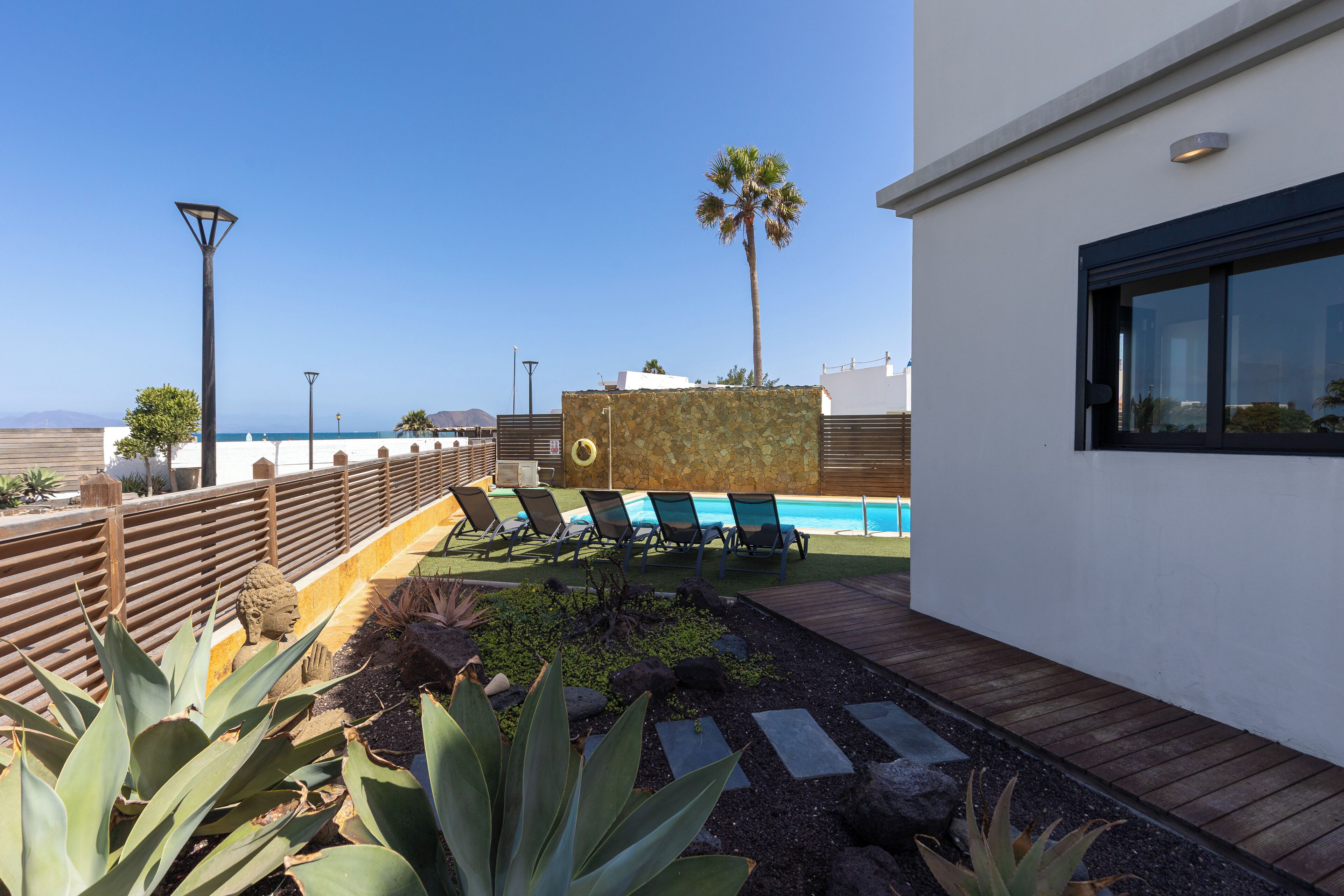Een modern buitenzwembad met ligbedden, een houten terras en uitzicht op de oceaan.