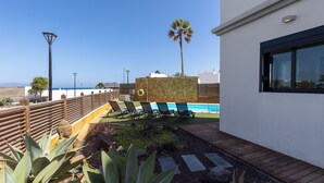 Uma área de piscina moderna ao ar livre, com espreguiçadeiras, um deck de madeira e vista para o oceano.