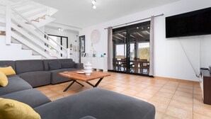 Uma sala de estar moderna com um sofá seccional cinza, uma mesa de centro de madeira e uma escada que dá para uma área externa.