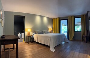 Un dormitorio con cama, lámparas de noche, mesitas de noche, una mesa de madera y una ventana con cortinas.