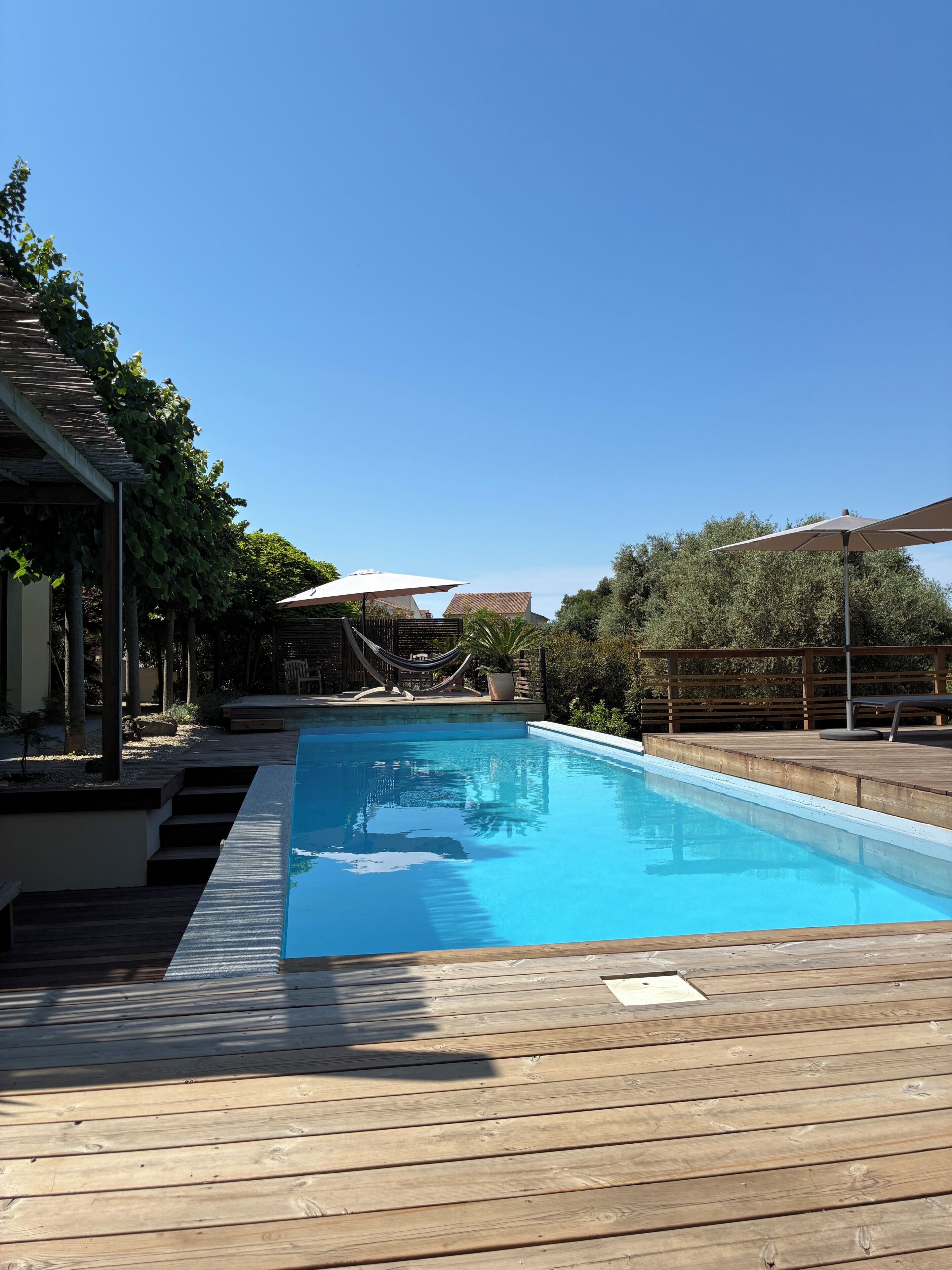 Une piscine avec une terrasse en bois, un hamac et une pergola.