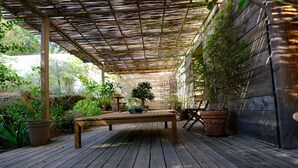 A wooden deck with a pergola, potted plants, and a bench.