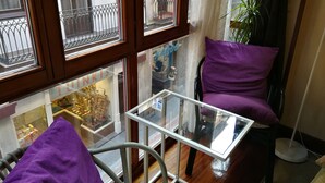 Rincón de una habitación con una mesa de vidrio, una silla morada y vista a una tienda llamada "TUNKIS" a través de una ventana.