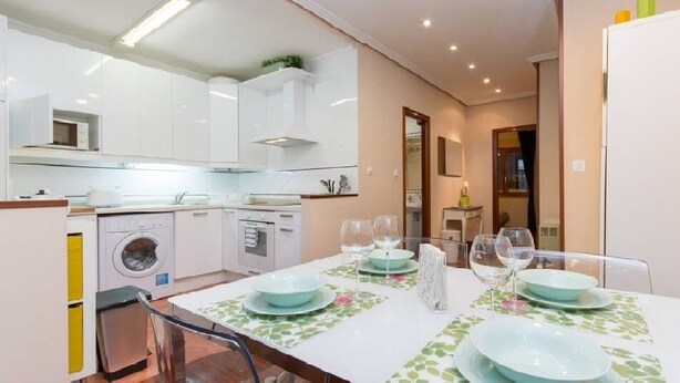 Una cocina moderna con armarios blancos, lavadora y comedor con mesa dispuesta para cuatro.