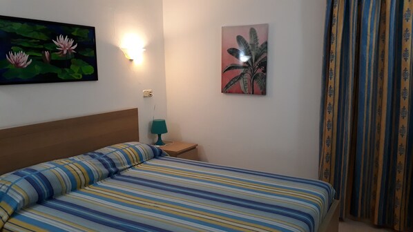 Una habitación de hotel con una cama, una mesita de noche, una lámpara y dos cuadros colgados en la pared.