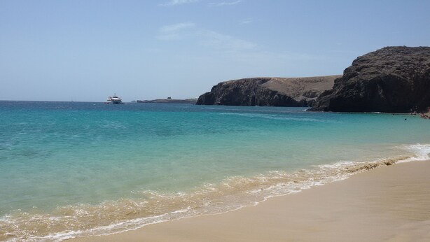 A beach with clear turquoise water, a sandy shore, and a rocky cliff.