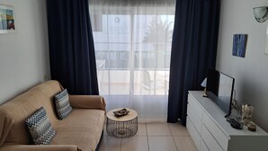 A modern living room with a beige sofa, a small round table, a flat-screen TV, and a white dresser.