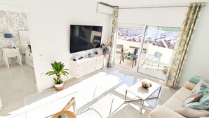 En moderne stue med et fladskærms-tv, et spiseområde med et glasbord og en sofa med hynder.