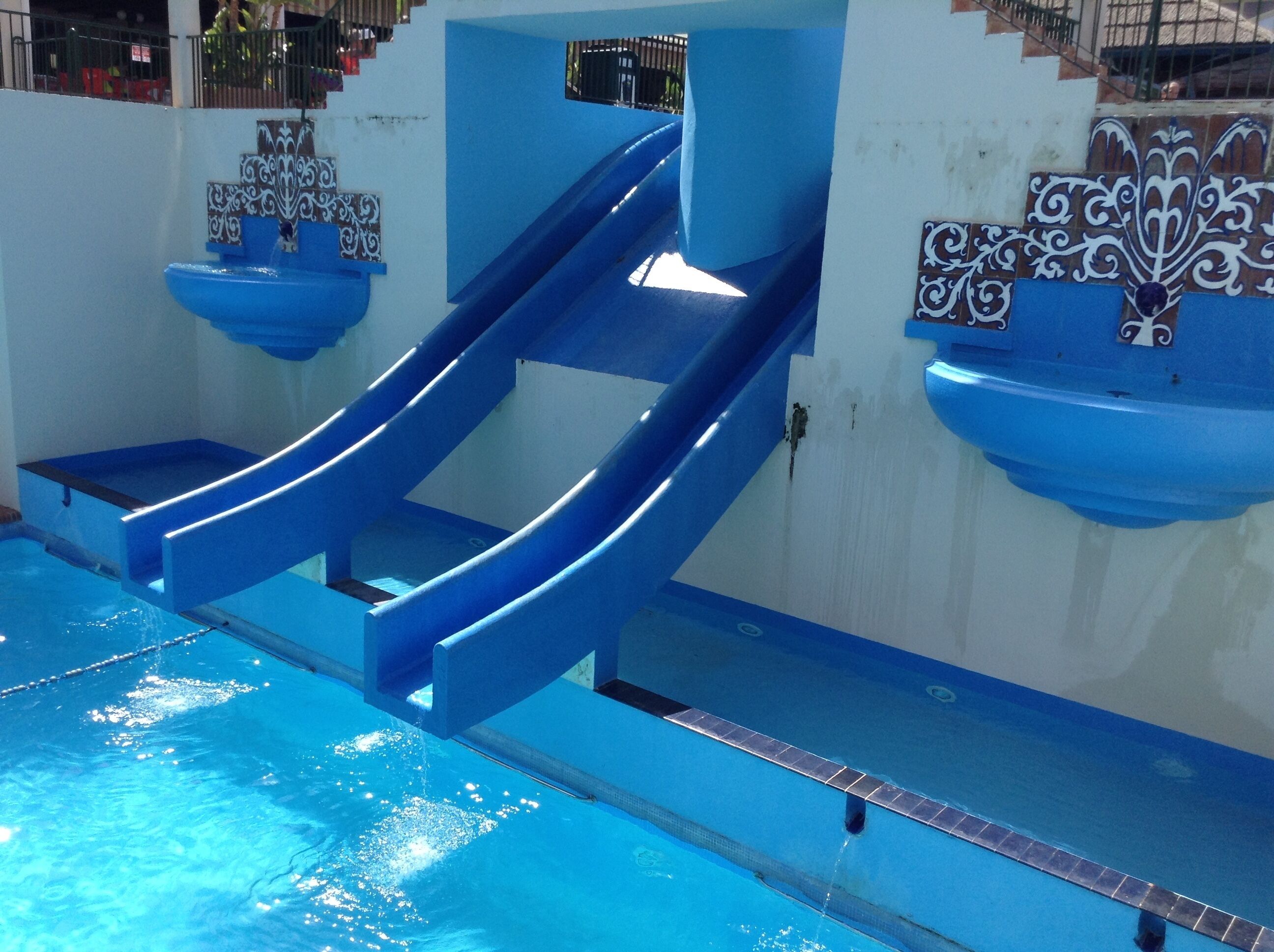 A blue water slide in a swimming pool area with tiled walls and a clear pool.