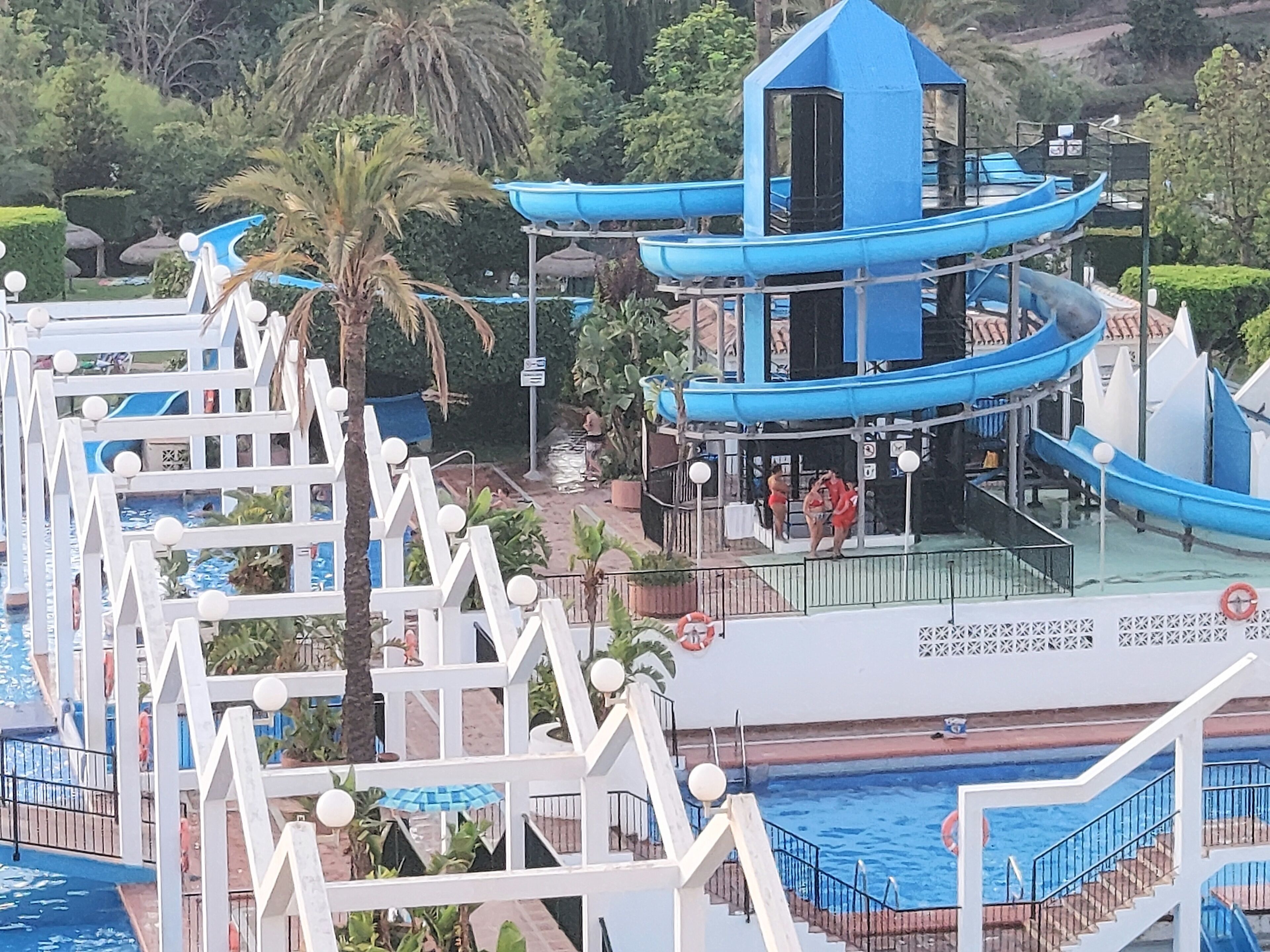 Parque acuático con múltiples toboganes y piscinas, rodeado de palmeras y un edificio azul.