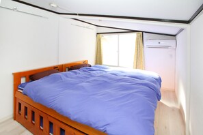 A bedroom with a wooden bed, a window with curtains, and an air conditioning unit.