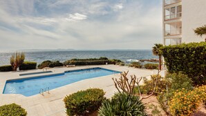 Una piscina con vistas al mar, rodeada de vegetación y un edificio con balcones.