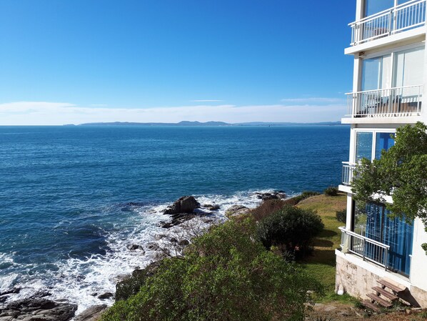 A coastal building with a balcony overlooking the ocean. - To your health, feet in the water (Roses)