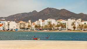 Un paisaje urbano costero con edificios, una playa y montañas al fondo.