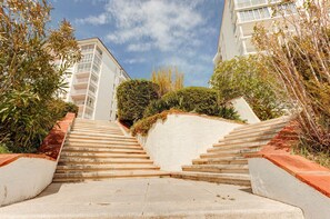 A staircase leading to a building with balconies, surrounded by greenery and a clear sky.