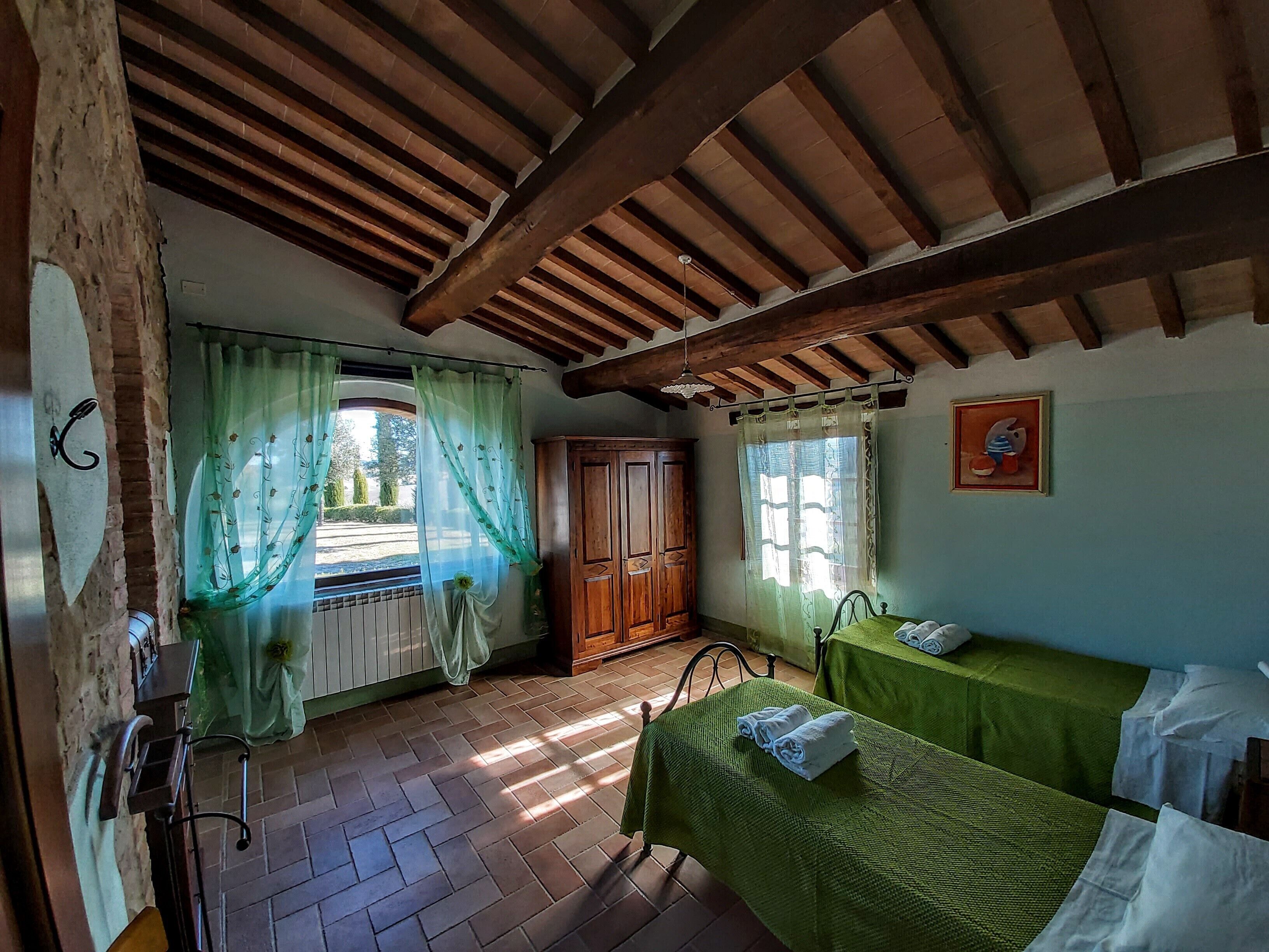 A room with a wooden ceiling, a bed with a green bedspread, a wooden wardrobe, and a window with curtains.
