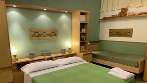 Un dormitorio con dos camas, una mesita de noche con lámpara, una estantería con libros y objetos decorativos, y un cuadro en la pared.