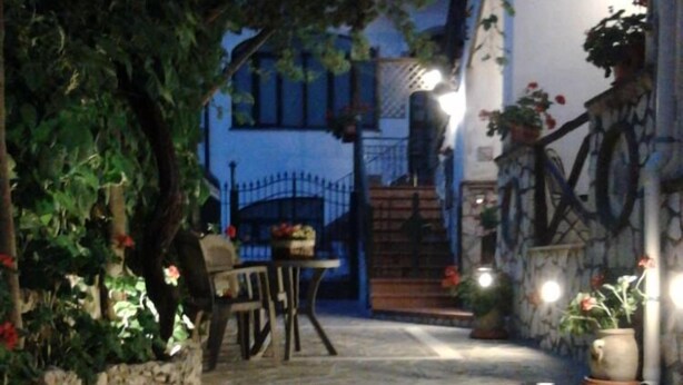 Un patio empedrado con una mesa y sillas, rodeado de plantas y un muro de piedra.