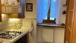 Una cocina con estufa a gas, armarios de madera, una ventana con cortina y un radiador.