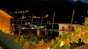 Vista nocturna de una zona montañosa con un edificio iluminado en primer plano y una luna brillante en el cielo.