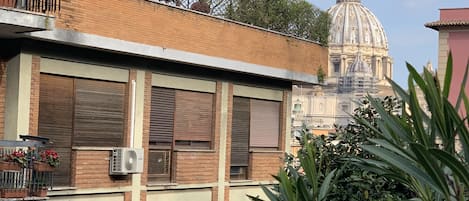 A building with a brick facade, multiple windows with shutters, and a balcony with potted plants.