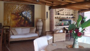 Ein gemütlicher Wohnbereich mit einer Couch, Korbstühlen, einem Tisch mit Blumenvase und einem großen abstrakten Gemälde an der Wand.