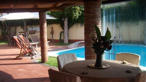 Eine Terrassenfläche mit einem runden Tisch, Stühlen, einer Vase mit Blumen und Blick auf einen Swimmingpool.