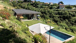 A modern house with a swimming pool, surrounded by lush greenery and hills.