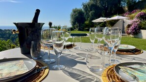 A table set for a meal with wine glasses, plates, and cutlery, overlooking a scenic landscape.