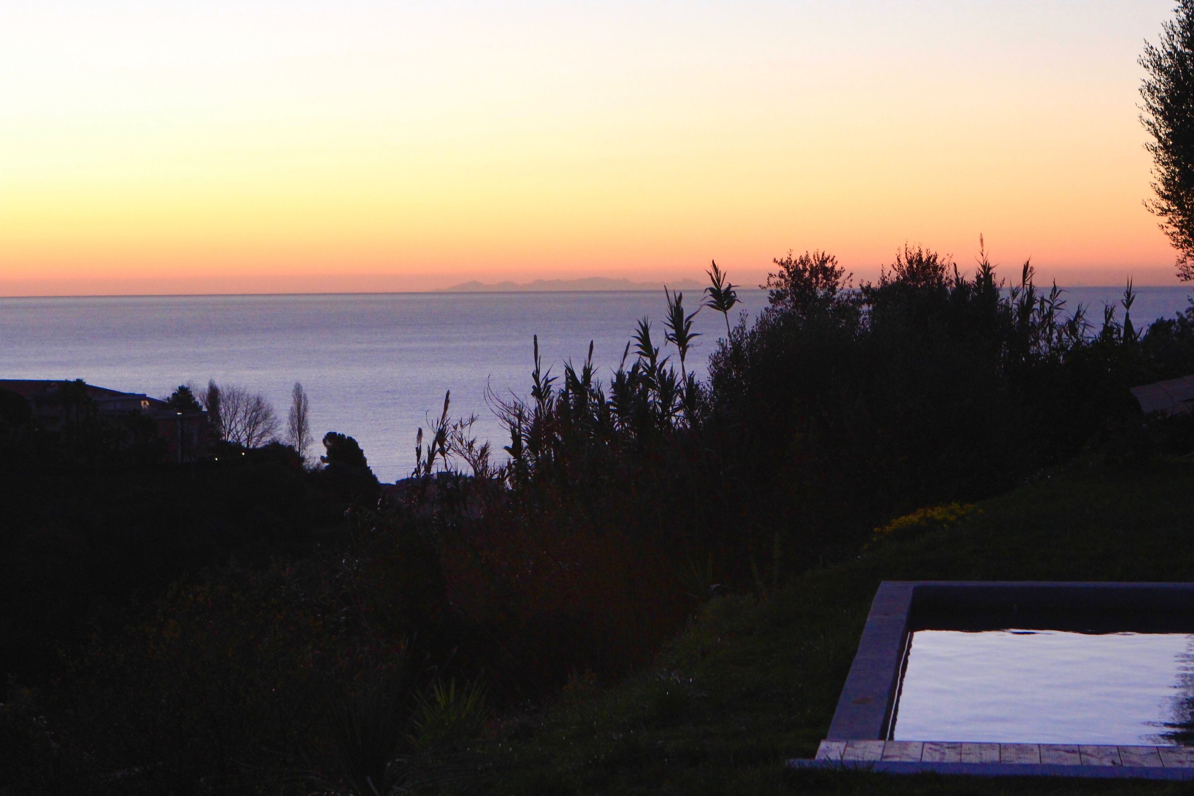 A view of a body of water at sunset with a pool in the foreground.